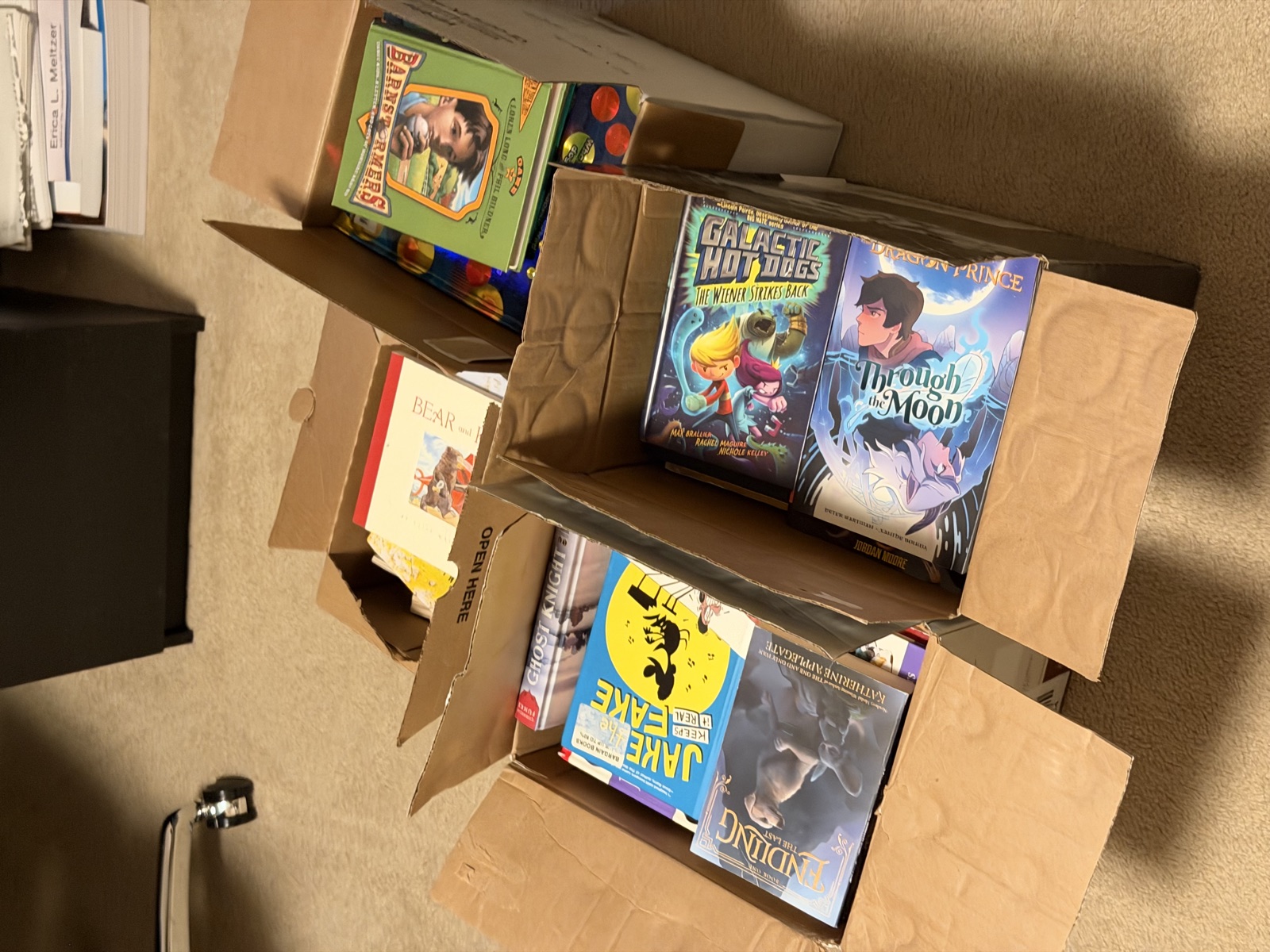 Four open boxes of sorted children's books on a floor at home